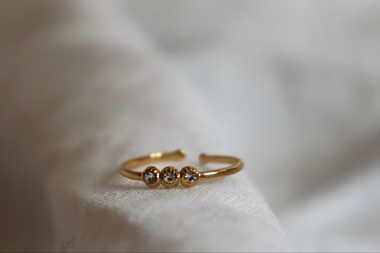 Anello 3 Dots regolabile in oro con tre zirconi su sfondo grigio
